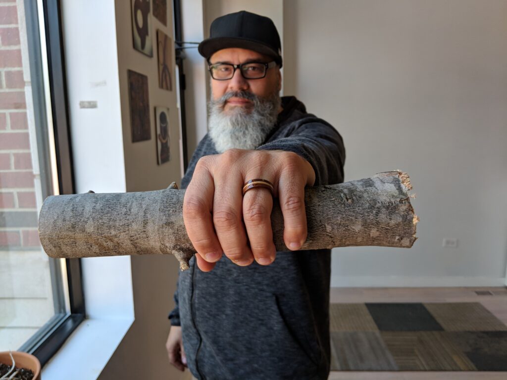 Gustav Reyes holding a branch with a finished wood ring, connecting raw material to the Simply Wood Rings process.